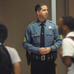 A police officer serving as a school resource officer stands in a school hallway.