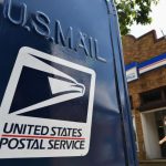 A United States Postal Service mailbox with a post office building in the background