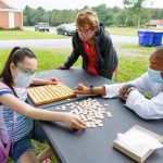 Two special education teachers works with a student on the lawn outside her house