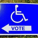 A sign with the International Symbol of Access and an arrow with VOTE written on it