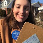 Jessica Benham, a candidate for a Pennsylvania congressional seat who has disclosed she is bisexual and has autism, stands in a neighborhood with a clipboard and campaign pin fixed to her sweatshirt.