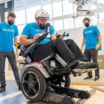 A man uses an experimental powered wheelchair while a team of engineers and researchers watch.