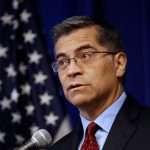 Xavier Becerra, the attorney general of California, stands with an American flag in the background