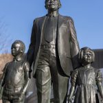 A statue of two children flanking Louis Redding, educational equity advocate, in a suit. Redding rests a hand on each child's shoulder