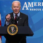 President Joe Biden speaks at a podium while behind him words read American Rescue Plan