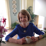 Alecia LaScala is an older woman with a brownish bob. She leans on a counter, holding a mug.