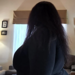 Kesha Williams is shown in profile. Her face is turned away from the camera so that only her long, dark hair is visible. She may be standing in her home, with pale walls, with simple black and white framed photos.