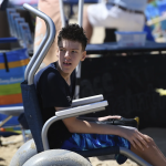 Jamie Oosterhaus sits in a beach chair while wearing swim trunks and a rash guard. He is a lanky teenager with short dark hair.