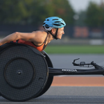 Susannah Scaroni leans forward, facing the sun, in her racing wheelchair.