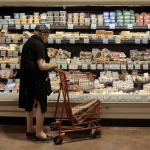 An older shopper browses in the cheese case at a New York supermarket.