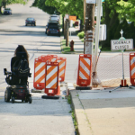 Anomie Fatale, in a powerchair, maneuvers around the closed sidewalk at the intersection of Port Royal and Henry avenues.