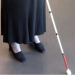Feet of a person in a skirt using a white cane.