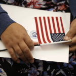A darker-skinned hand holds a US flag with a certificate from the CIS