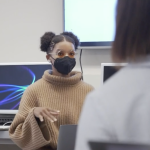 Screenshot from video shows a UC Berkeley student wearing a mask with hair in afro puffs speaking to someone blurry in the foreground.