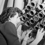 A vintage photo of a women operating pneumatic tubes.
