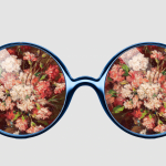 A pair of round-framed blue glasses with a painting of flowers in the lenses.