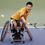Shingo Kunieda of Japan returns a shot during the men’s wheelchair singles final of the U.S. Open. Kuneida wears a yellow tennis shirt, leans far to the left. He grimaces with his mouth open in effort.