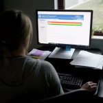 A person sits at a computer. On the screen is a Department of Human Services Allegheny County, Pennsylvania web portal.
