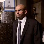 US Senator John Fetterman is a tall man with a bald head, strong eyebrows and a beard. He wears a suit and tie.