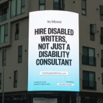 A billboard on the corner of a building reads: Hire Disabled Writers, not just a disability consultant