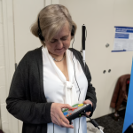 An older woman with short blond hair uses an electronic controller with braille to vote.