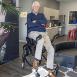 Garrett Brown, a tall older man, sits on his invention, a hybrid wheelchair-walker that supports a range of mobility.