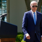President Biden in his signature aviator sunglasses walks away from a podium outside of the White House
