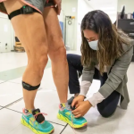 Biomechanics and movement science doctoral student Fany Alvarado is outfitting study participant Jennifer Kraut with wearable sensors on her feet and legs
