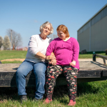 Marilyn Lesmeister and her daughter Samantha "Sammee" Lesmeister sit on a flatbed trailer sitting on a farm