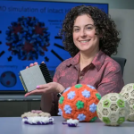 Jodi Hadden-Perilla poses with crochet models of viruses and a piece of computer equipment