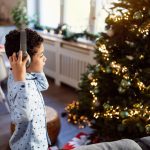 A boy wearing headphones looks at a Christmas tree.